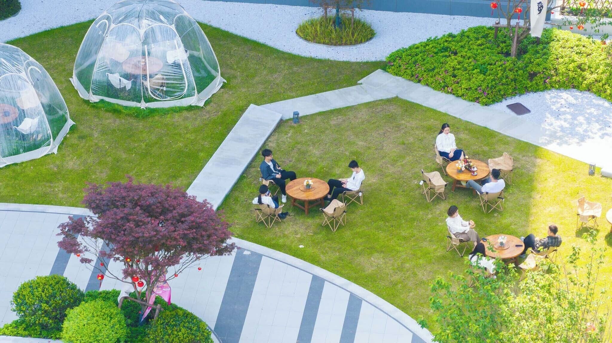 Um pátio com estruturas em cúpula transparente, áreas de estar ao ar livre e uma árvore central decorada com enfeites vermelhos.