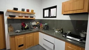 A compact kitchen with wooden cabinets, a countertop, and a stove. - Kali Code Home (Yogyakarta)