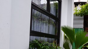 A building with a large window, potted plants, and a concrete pathway. - Kali Code Home (Yogyakarta)