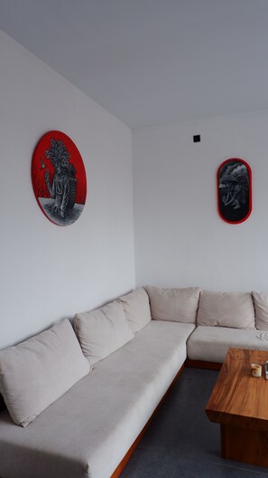 A modern living room with a beige sectional sofa, a wooden coffee table, and two wall-mounted artworks.