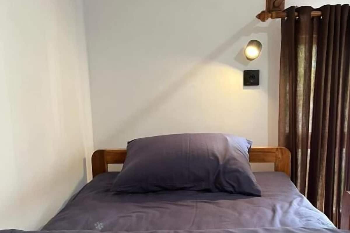 Una cama individual con cabecera de madera, colchón gris y una sola almohada.