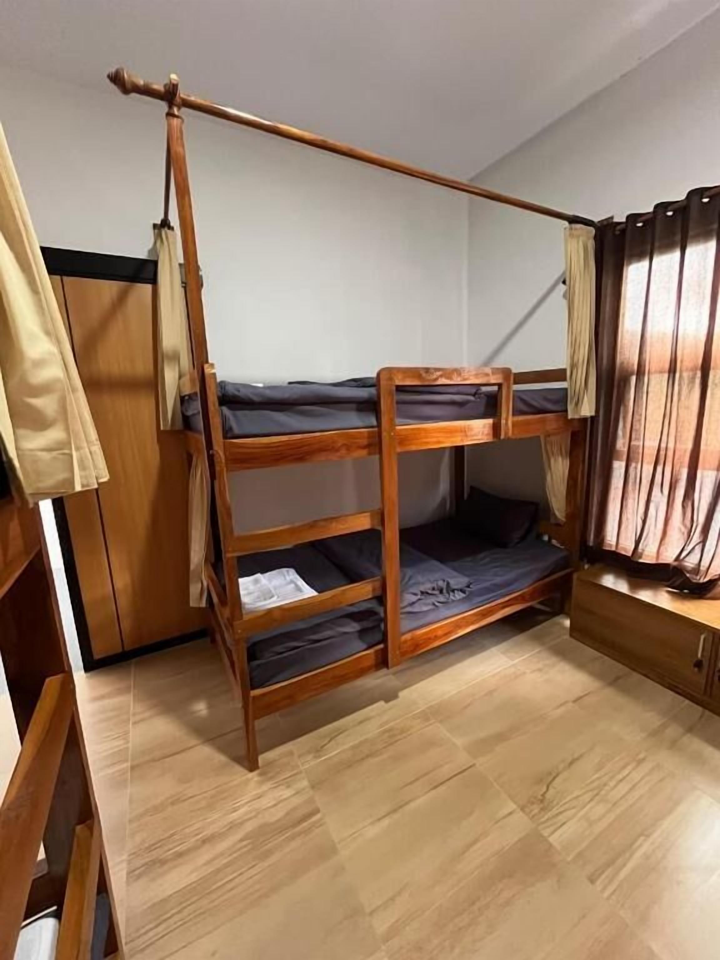 A bunk bed room with wooden flooring, a wardrobe, and a curtain.
