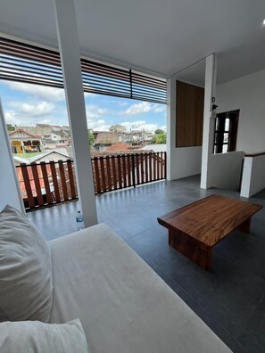 Un salon moderne avec un canapé blanc, une table basse en bois et de grandes fenêtres donnant sur un quartier résidentiel.