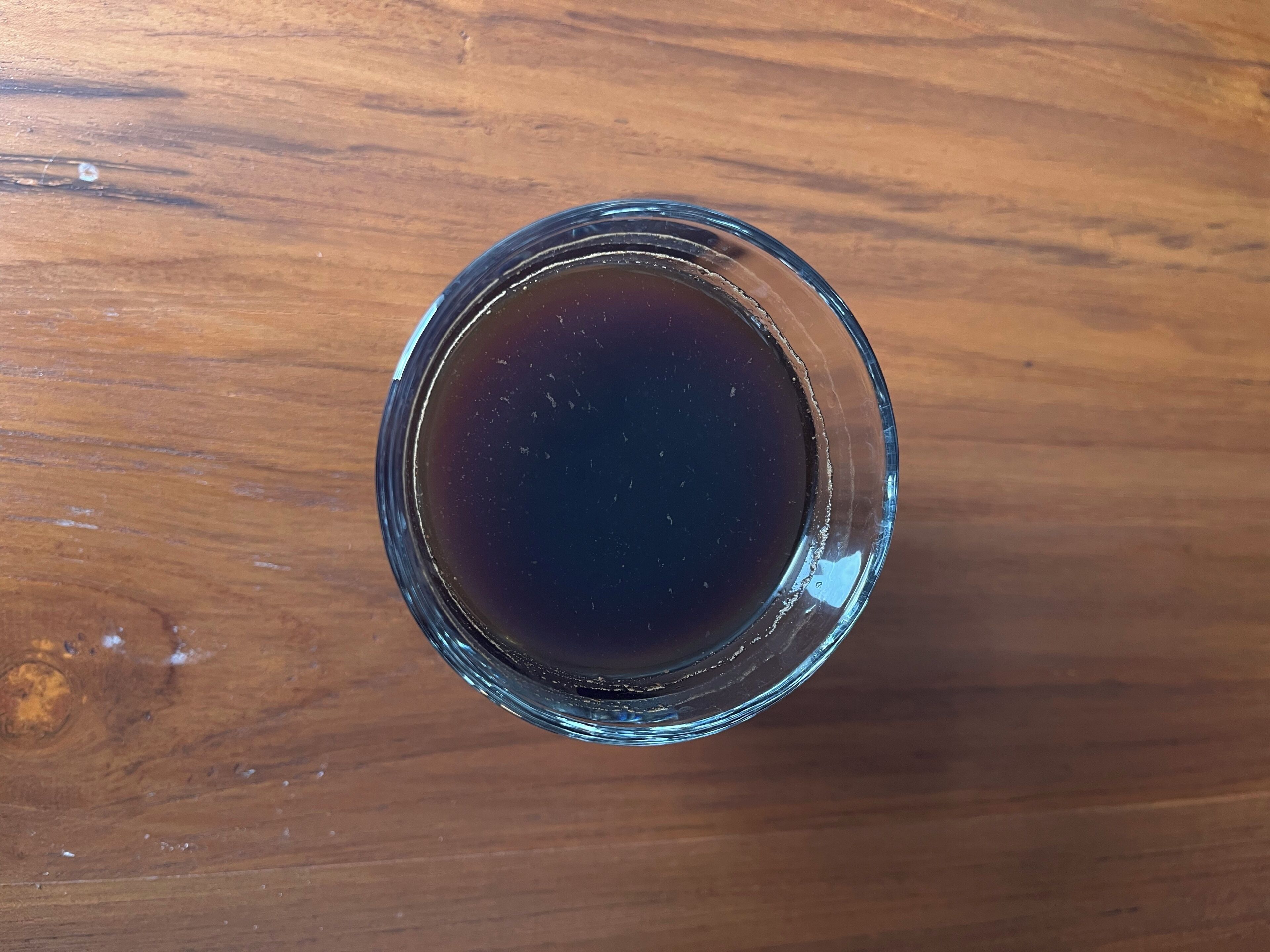 Un vaso de líquido oscuro sobre una superficie de madera.
