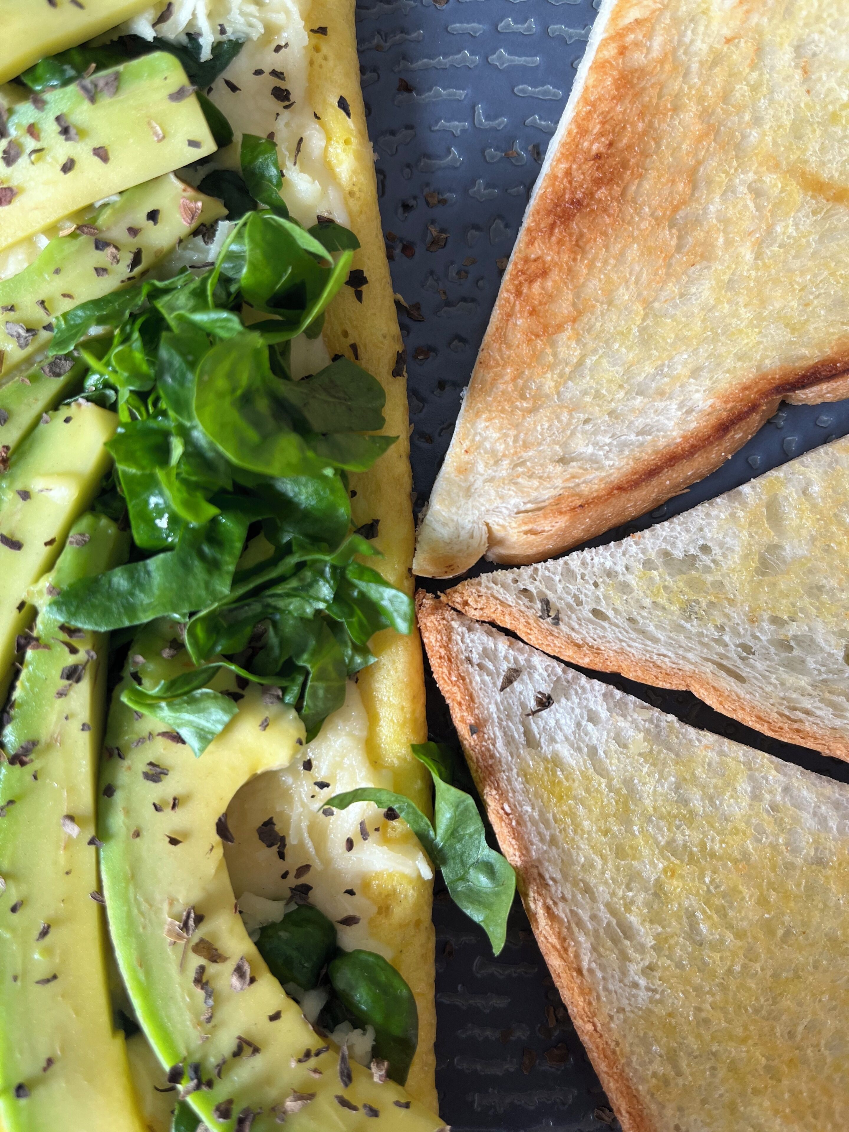 A breakfast plate with avocado slices, spinach, and toasted bread.