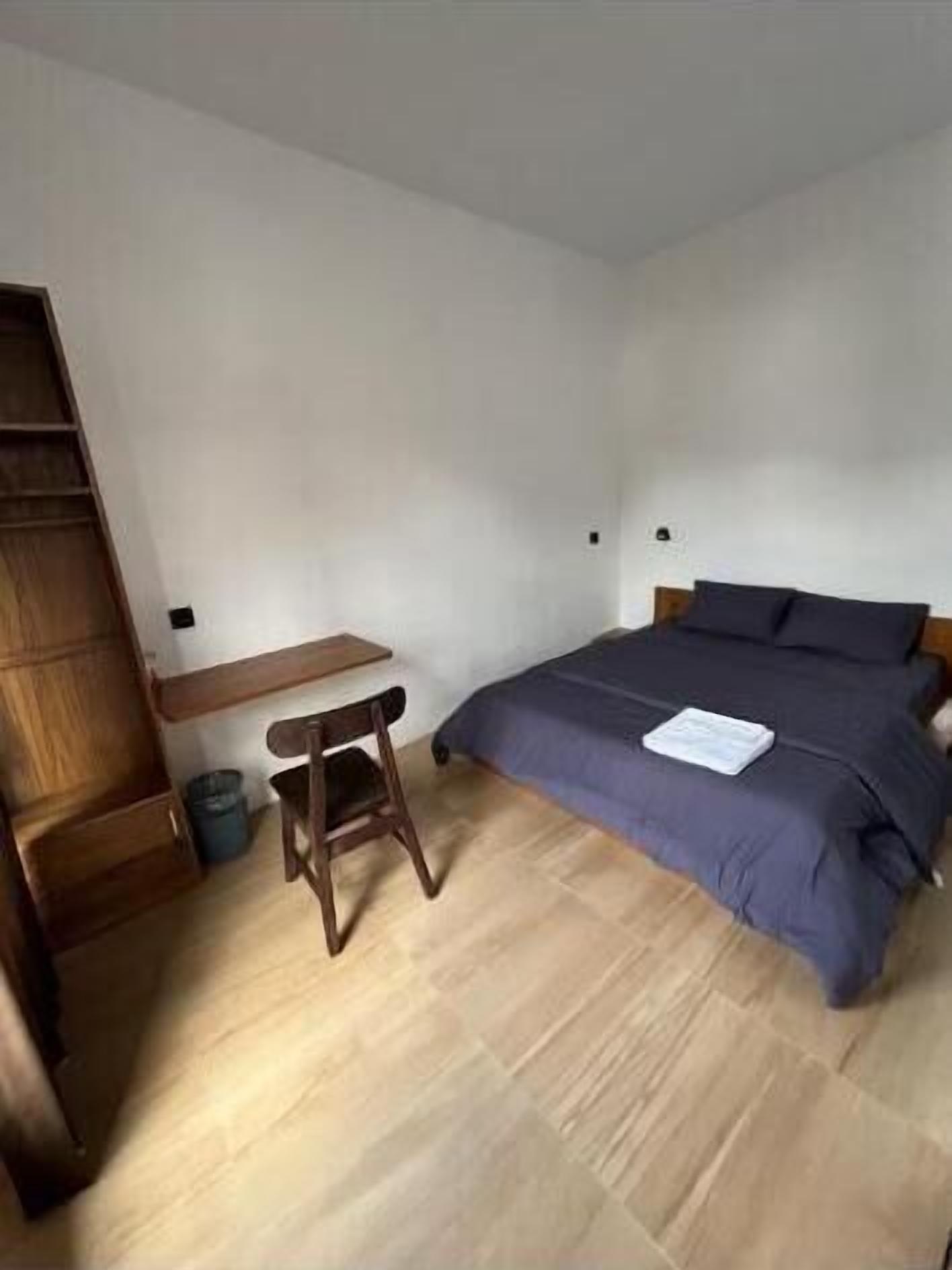A bedroom with a bed, a wooden desk, and a small stool.