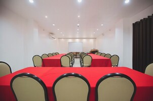 Un salón de conferencias con una larga mesa, varias sillas, una pantalla de proyector y un atril.