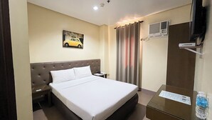 A hotel room with a bed, a nightstand, a telephone, a painting of a car, a window with curtains, an air conditioning unit, and a small table with a water bottle. - Hotel 801 Inc. (Cagayan de Oro)