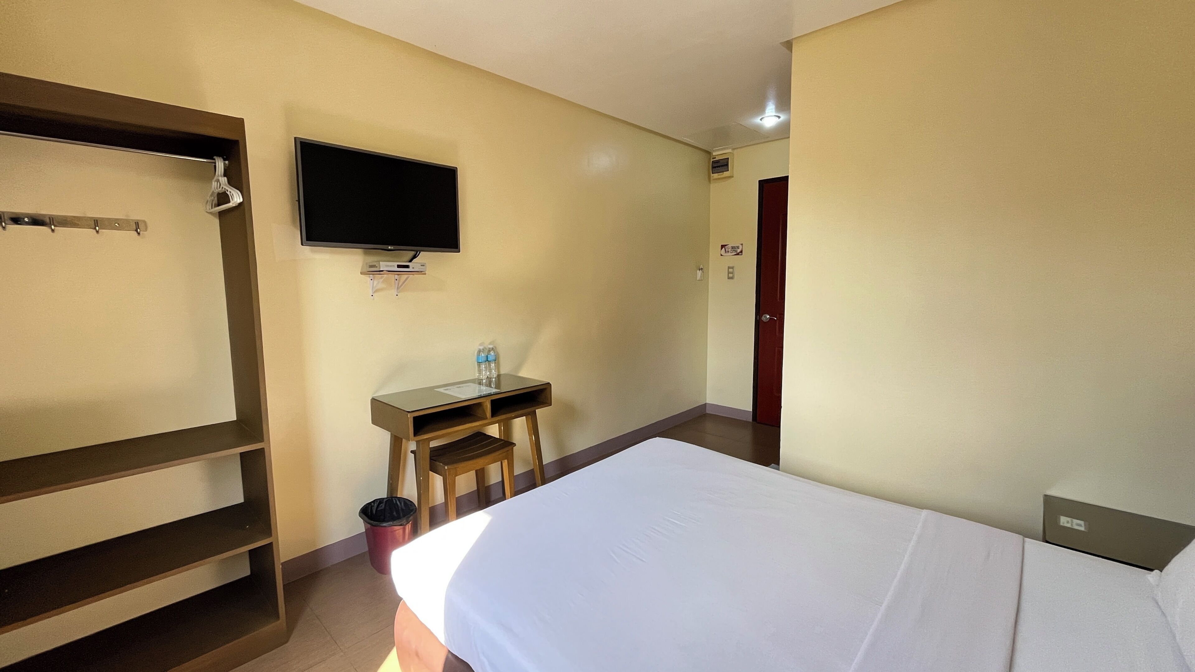 Ein Hotelzimmer mit Bett, Wandfernseher, Schreibtisch mit Stuhl und Kleiderhaken.