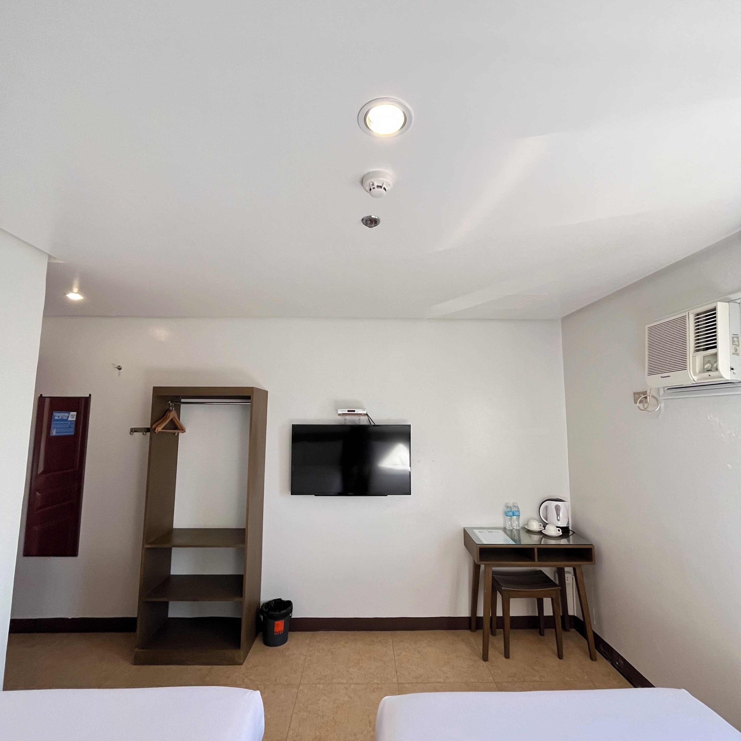 A hotel room with a bed, a desk with a chair, a television, and an air conditioning unit.