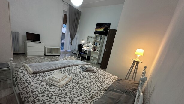 A bedroom with a bed, a desk, a chair, a TV, a wardrobe, and a lamp. - Bright central apartment (foggia)