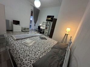 A bedroom with a bed, a desk, a chair, a TV, a wardrobe, and a lamp.