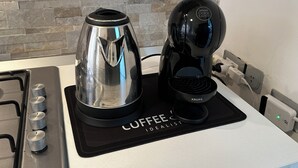 A coffee maker and a kettle on a black mat labeled 'COFFEE Idealist' in a kitchen with a stone backsplash. - Bright central apartment (foggia)