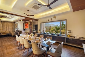 A dining area with a long table, chairs, ceiling fans, and a view of the outdoors. - Mountain Creek 7BHK Villa by ELIVAAS (Udaipur)