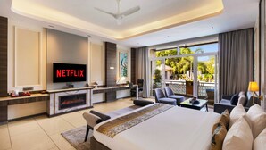 A modern hotel room with a large bed, a TV mounted on the wall, a fireplace, a balcony with outdoor seating, and a ceiling fan. - Mountain Creek 7BHK Villa by ELIVAAS (Udaipur)