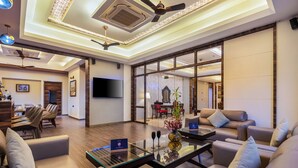 A modern hotel lobby with a seating area, a flat-screen TV, and a ceiling fan. - Mountain Creek 7BHK Villa by ELIVAAS (Udaipur)