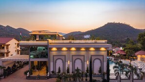 A hotel with a modern design, featuring a rooftop terrace, a swimming pool, and a view of the surrounding hills. - Mountain Creek 7BHK Villa by ELIVAAS (Udaipur)