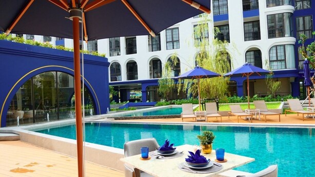 Zona de piscina con mesa lista para comer, sillas de descanso y sombrillas.