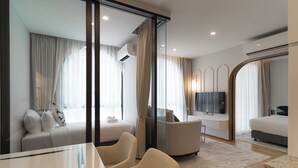 Una habitación de hotel moderna con un separador de vidrio, un sofá, un televisor, una cama y un escritorio con sillas.