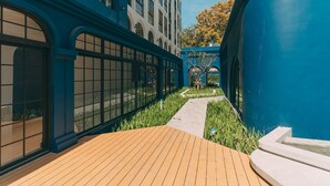 Un edificio moderno con amplios ventanales, una terraza de madera y una pared exterior azul.