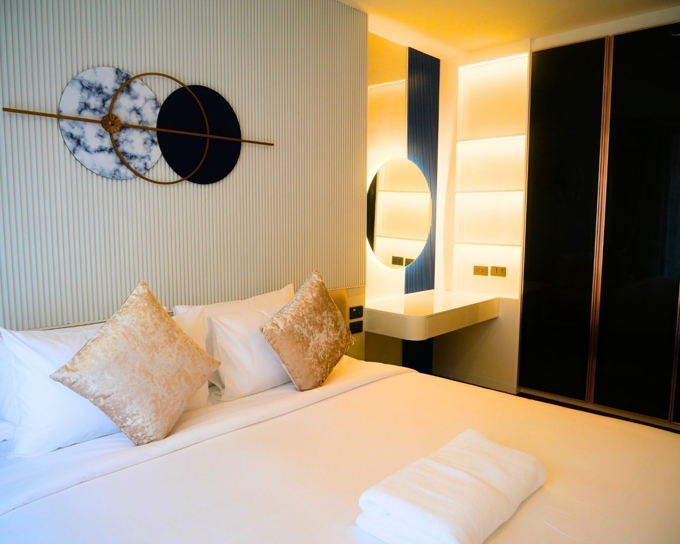 A hotel room with a bed, pillows, a bedside table, a mirror, and a wardrobe.