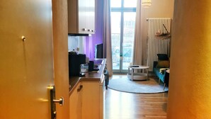 Un pasillo estrecho que conduce a una cocina con ventana, un radiador y un comedor con mesa y sillas.