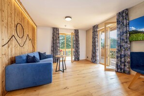 Ein modernes Wohnzimmer mit einem blauen Sofa, Holzvertäfelung, einem kleinen Tisch mit einer Vase und einem großen Fenster mit Vorhängen.