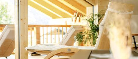 A wooden-framed lounge chair with a cushion, positioned near a window with a view of the outdoors.