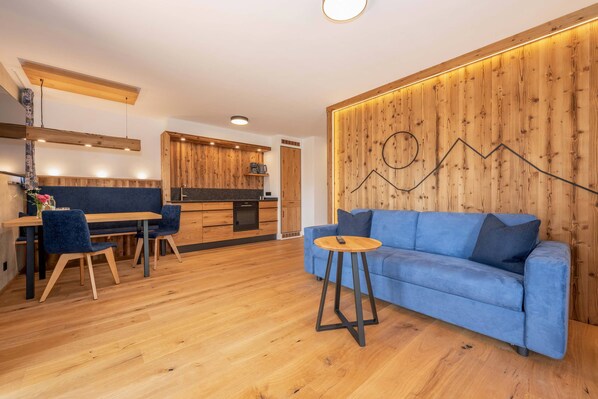 Ein modernes Interieur mit einem Essbereich aus Holz, einem blauen Sofa und einer Küche mit Holzschränken.