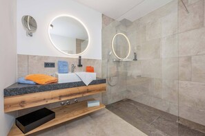 Ein modernes Badezimmer mit Waschtisch, zwei Spiegeln, einer Dusche und einem Handtuchhalter.