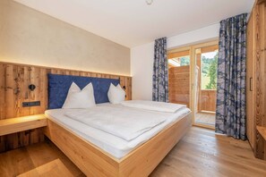 Ein Schlafzimmer mit Holzkopfstütze, einem Bett mit weißen Bettwäsche, einem Nachttisch aus Holz und einer Schiebetür zum Außenbereich.