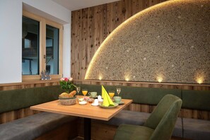 A dining area with a wooden wall, a table set with breakfast items, and a bench. - (4) First-floor vacation rental with a balcony /2 (Reit im Winkl)