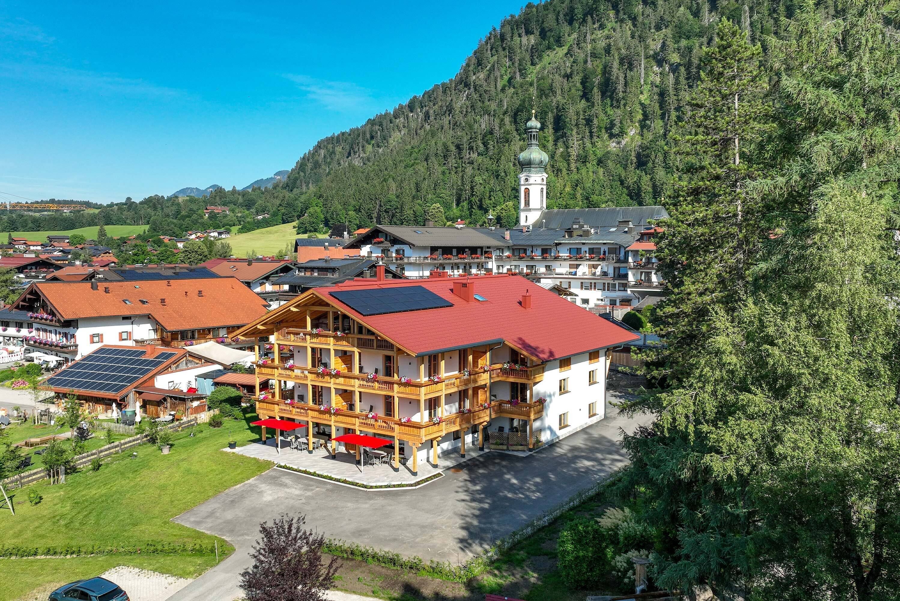 Um edifício com vários andares e telhado vermelho, cercado por vegetação e um cenário montanhoso.