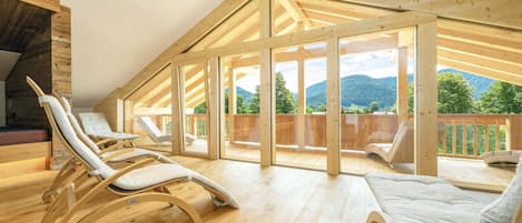 A spacious wooden interior with a sloped ceiling, large windows, and a view of a mountainous landscape.