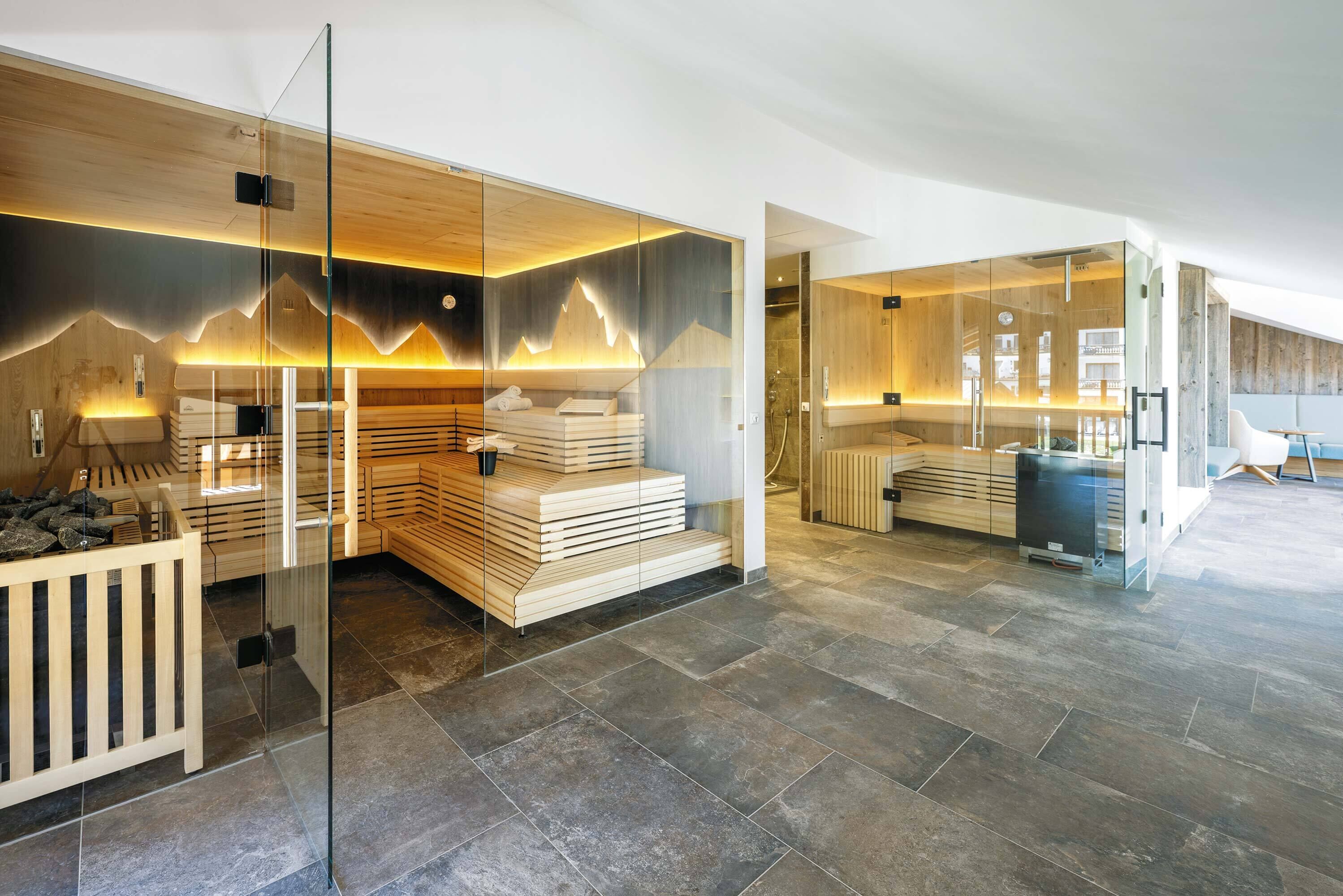 Een moderne spa met houten banken, glazen scheidingswanden en een vloer van stenen tegels.