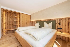 A bedroom with a wooden bed frame, two pillows, a bedside table, and a wardrobe with a built-in ladder. - (1) Vacation rental with a small terrace (Reit im Winkl)
