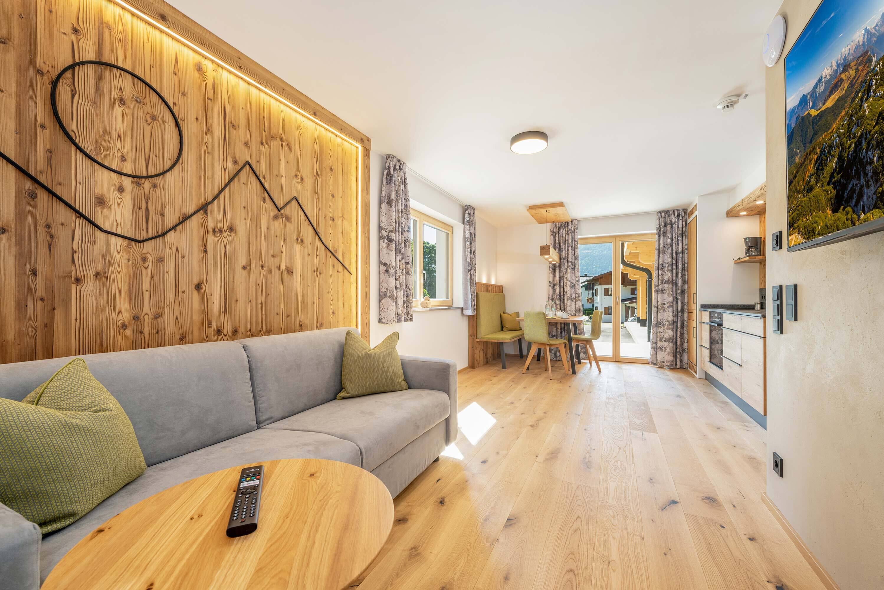 Een moderne woonkamer met een houten wandpaneel, een grijze bank, een ronde houten salontafel en een afstandsbediening op de tafel.
