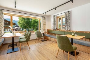 Een restaurant met houten vloeren, groene bekleding en grote ramen met uitzicht op het omliggende landschap.
