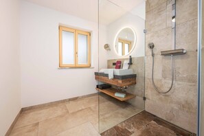 Een moderne badkamer met een douchecabine van glas, een wastafel met spiegel en een raam.