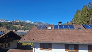 Un bâtiment doté d’un toit recouvert de tuiles brunes, de panneaux solaires et ayant une chaîne de montagnes en arrière-plan.