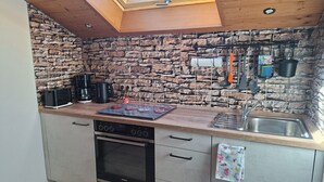 Une cuisine avec un mur en pierres apparentes derrière l’évier, un puits de lumière, un four Siemens et un plan de travail en bois.
