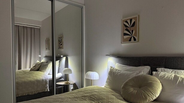 Hotellihuone, jossa on sänky, yöpöytävalaisimet, peili ja seinätaideteos.