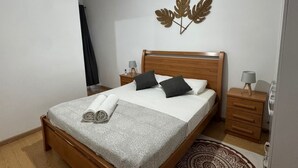 A bedroom with a wooden bed, a nightstand, a wall-mounted lamp, and a decorative leaf wall piece. - Cdas&Fav Apartment Grand baie Mauritius  (Grand Baie)