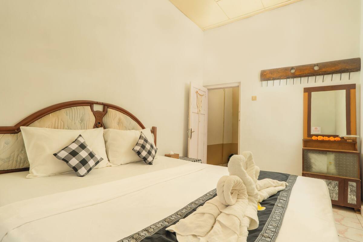 Een opgemaakt bed met kussens, een nachtkastje en een spiegel.