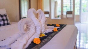 Ein Bett mit ordentlich gefalteten weißen Handtüchern, die in Herzform angeordnet sind, einem karierten Kopfkissen und einem Zierkissen mit orangefarbenen Blumen.