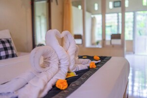 Una cama con toallas blancas dobladas con cuidado formando un corazón, una almohada de cuadros y una almohada decorativa con flores naranjas.