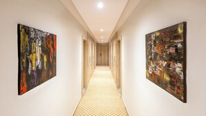 Un couloir aux murs ornés de peintures abstraites, doté d’un sol à motifs et d’un plafond pourvu d’un éclairage encastré.
