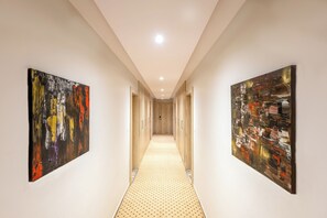 Een gang met abstracte schilderijen aan de wanden, een vloer met patroon en een plafond met inbouwspots.