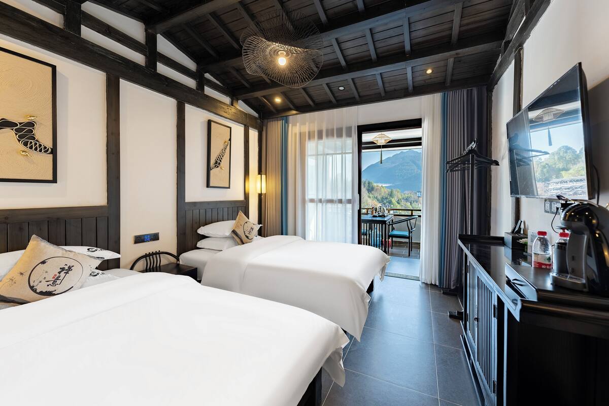 A hotel room with two beds, a TV, a balcony with a view, and a ceiling light fixture.