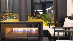 A wood-burning stove with a glass front, a black chair, and a view of a cityscape through a window. - 12C View Homestay (Xiangxi)